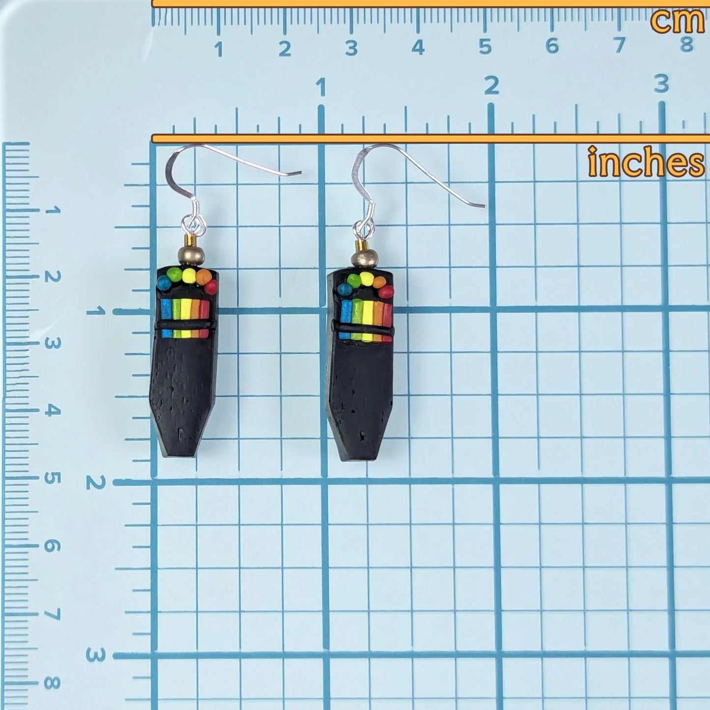 Pair of polymer clay earrings that look like EMF readers on a blue grid background with measurements.