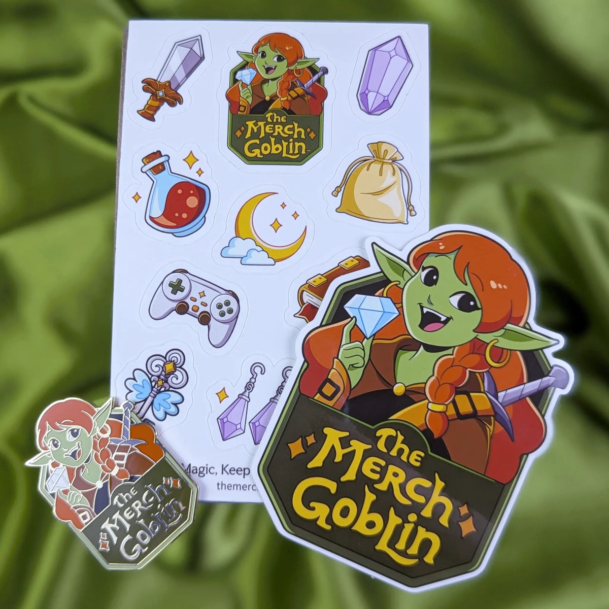 3 Item bundle of The Merch Goblin logo sticker, hard enamel pin, and a sheet of fantasy themed stickers including a sword, purple gem, potion bottle, moon game controller, magical book, sparkling jewelry, cute water sprite, flying key, a gold bag