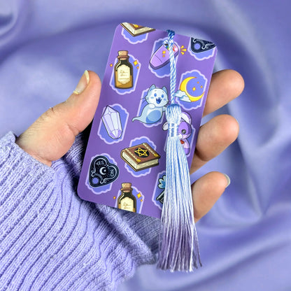 Purple bookmark with cute ghost hunter illustrations with tassel held by a hand against a matching purple background