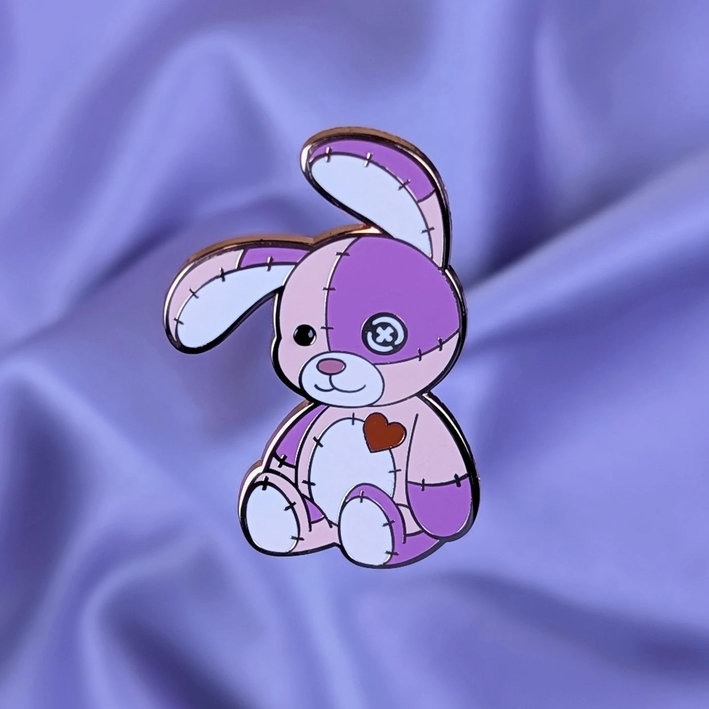 Pink and purple cute cursed stitched bunny hard enamel pin with rose gold metal, red heart, and button eye
