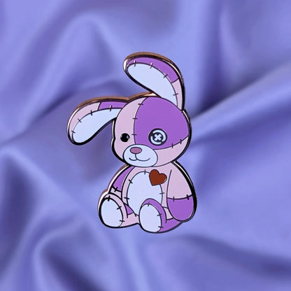 Pink and purple cute cursed stitched bunny hard enamel pin with rose gold metal, red heart, and button eye