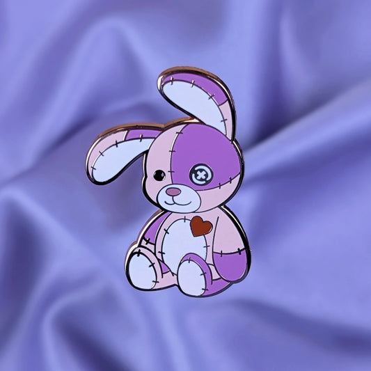 Pink and purple cute cursed stitched bunny hard enamel pin with rose gold metal, red heart, and button eye
