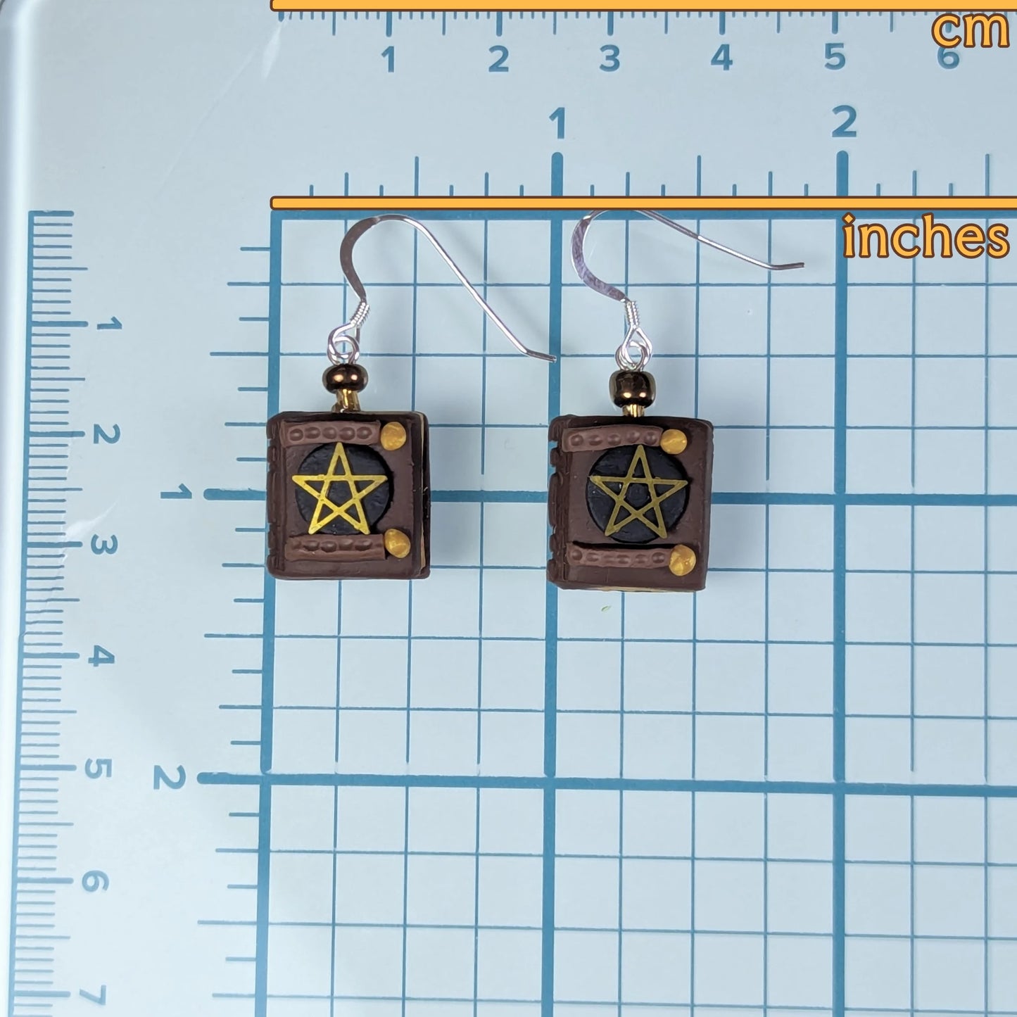 Pair of earrings with pentagram design on a grid background with measurements.