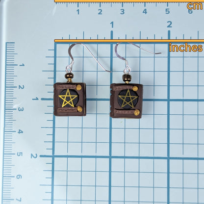 Pair of earrings with pentagram design on a grid background with measurements.