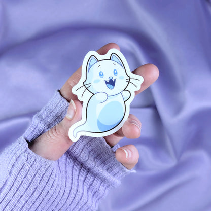 Hand holding a cute ghost cat sticker against a purple fabric background