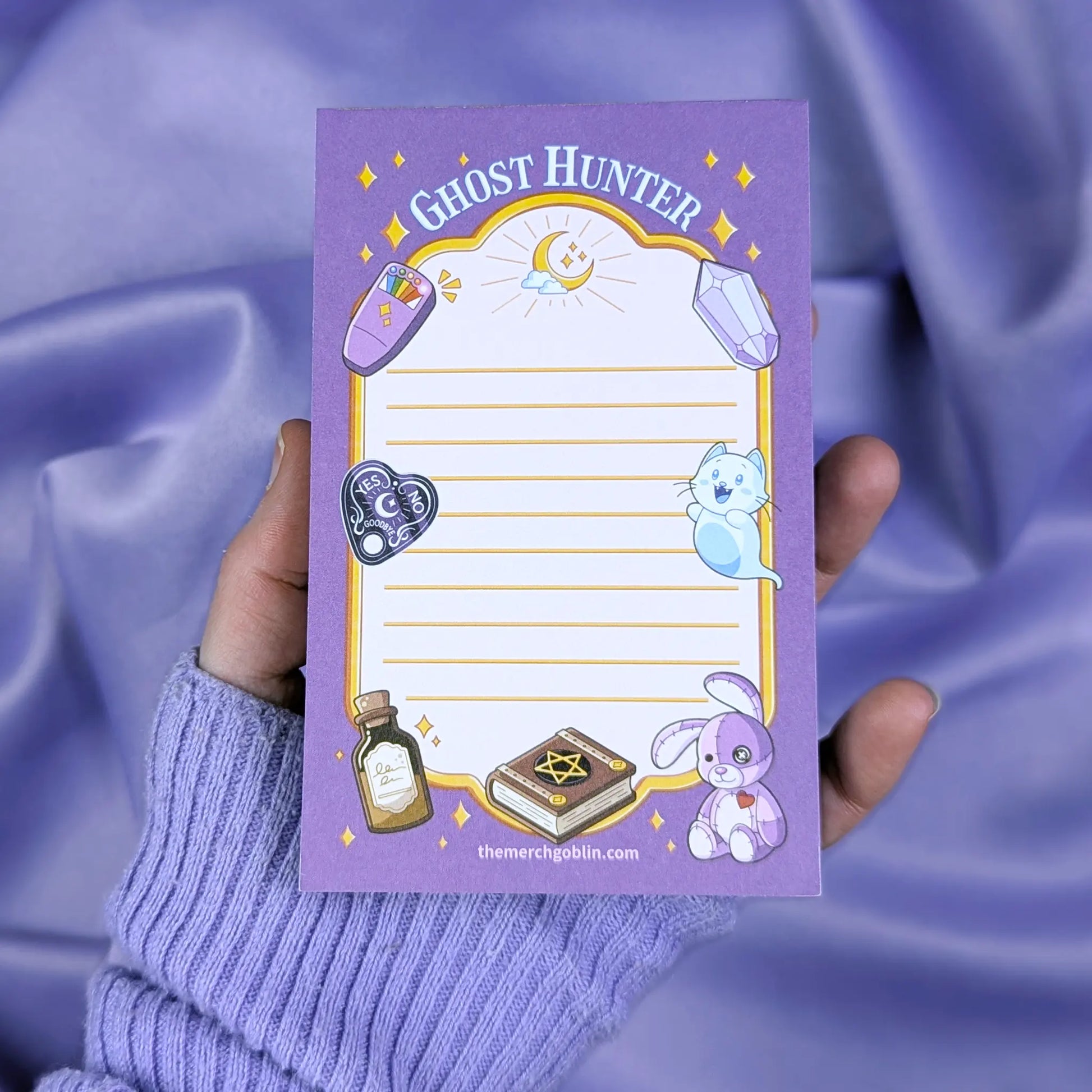 Notepad with 'Ghost Hunter' design held by a hand against a purple fabric background