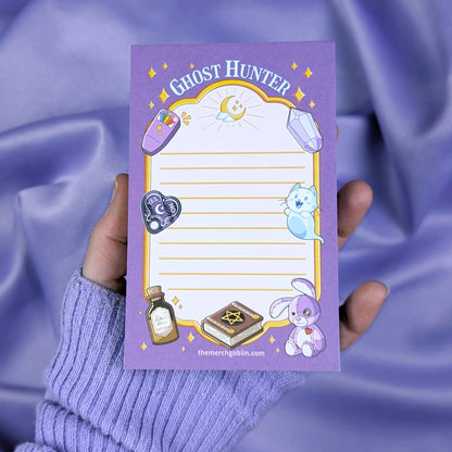 Notepad with 'Ghost Hunter' design held by a hand against a purple fabric background