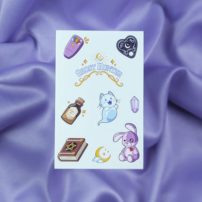 Sheet of ghost hunter themed stickers including an EMF ghost detector, spirit board planchette, Ghost Hunter sticker, sanity potion bottle, ghost cat, purple gem, spooky book, moon, and cursed stitched bunny