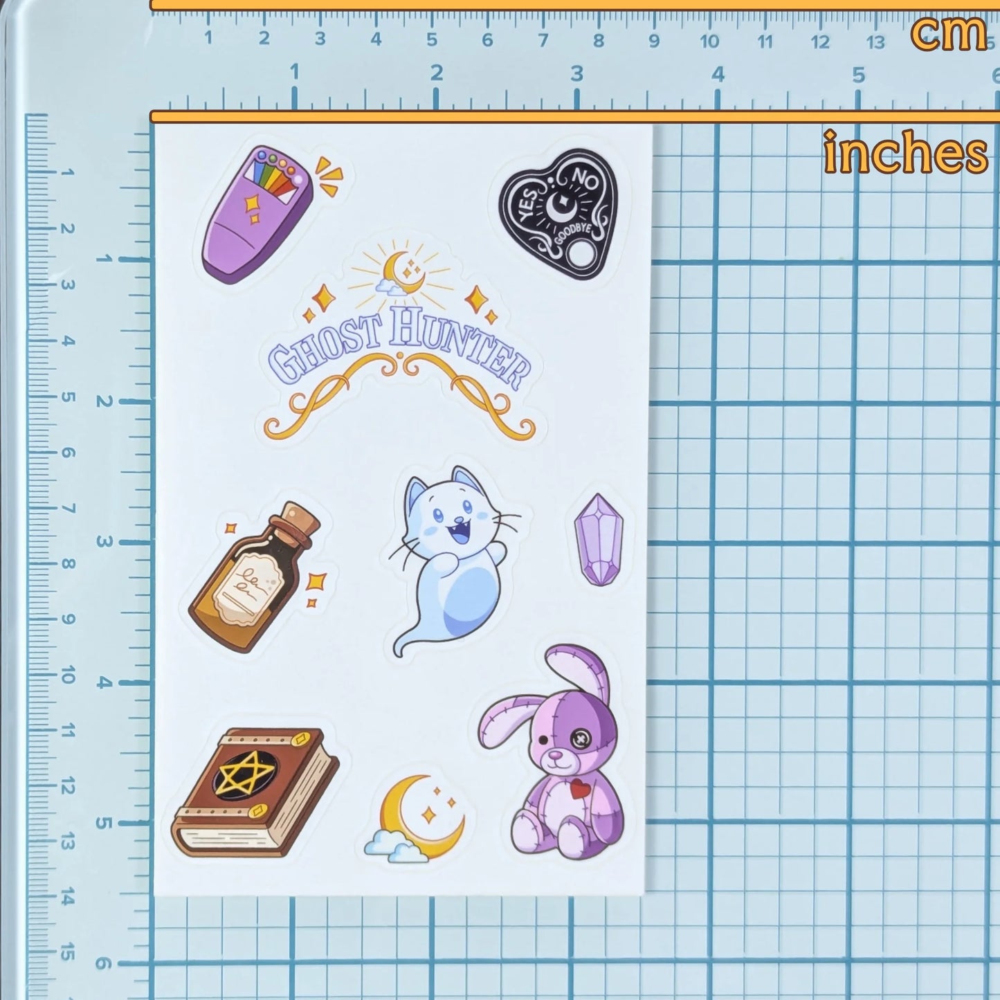 Sheet of stickers with cute illustrations of ghost huntering items on a grid background with ruler to show scale.