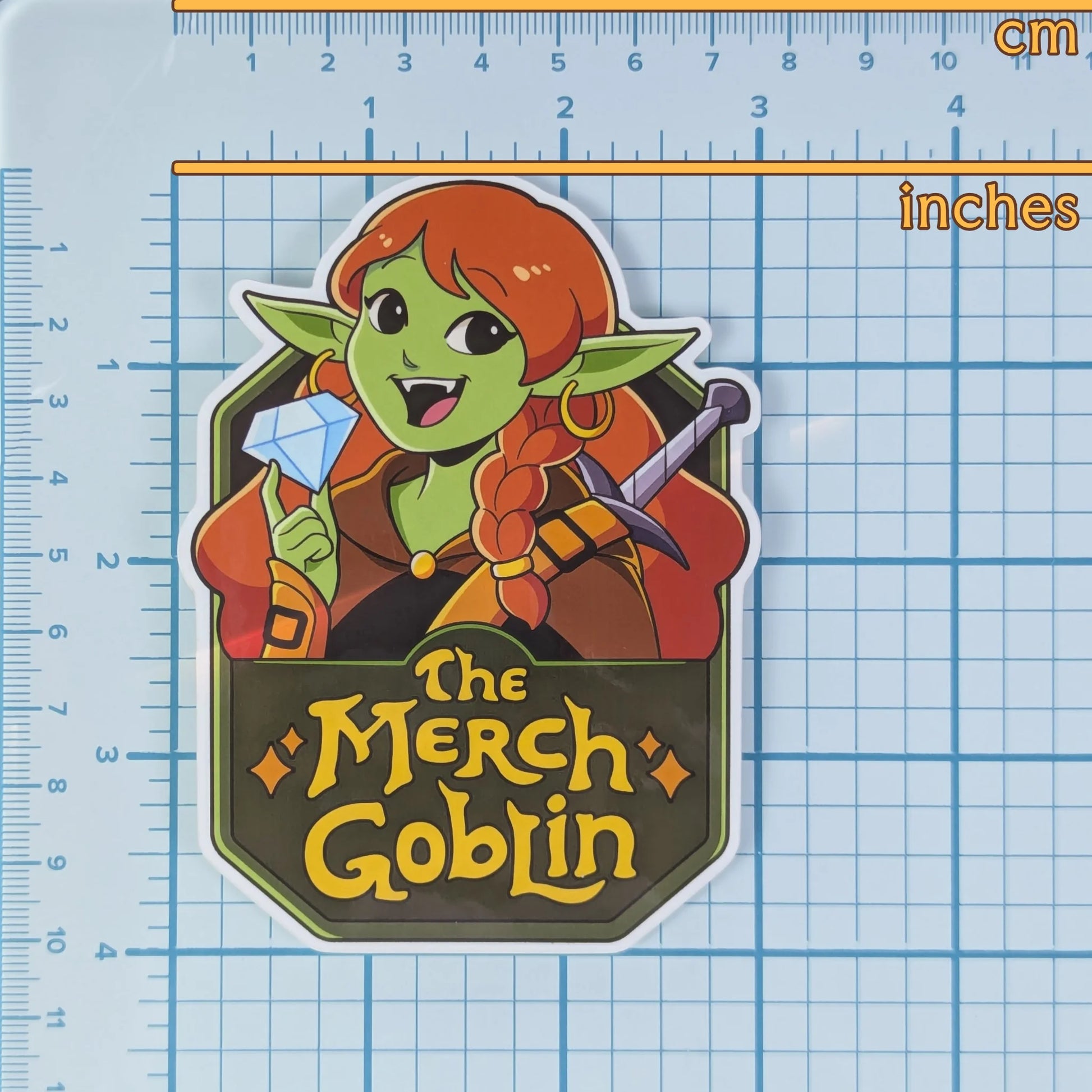 Sticker of 'The Merch Goblin' logo on a grid background to show measurements.