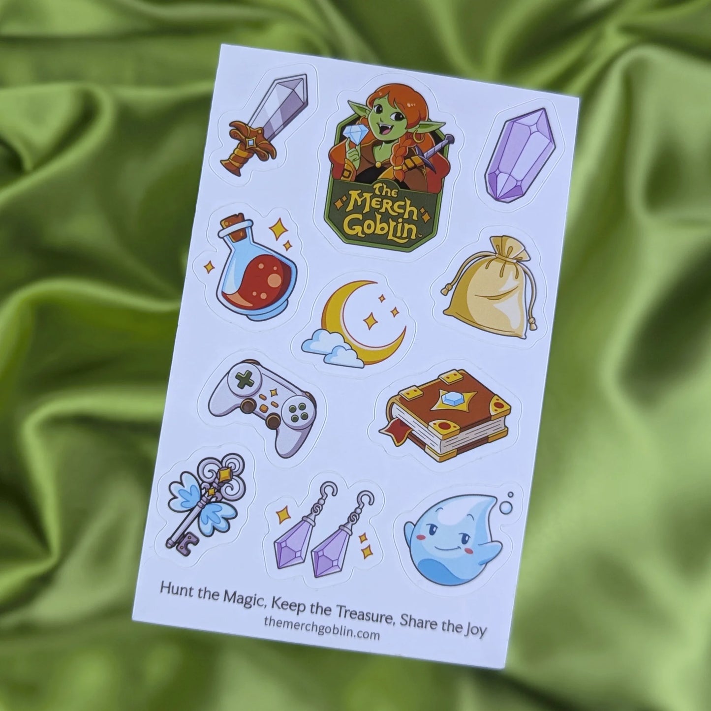 Sheet of fantasy themed stickers including a sword, purple gem, potion bottle, moon game controller, magical book, sparkling jewelry, cute water sprite, flying key, a gold bag, and The Merch Goblin logo