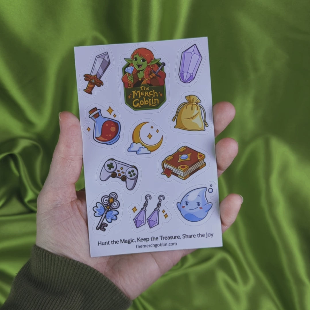 Video of a sheet of fantasy themed stickers including a sword, purple gem, potion bottle, moon game controller, magical book, sparkling jewelry, cute water sprite, flying key, a gold bag, and The Merch Goblin logo