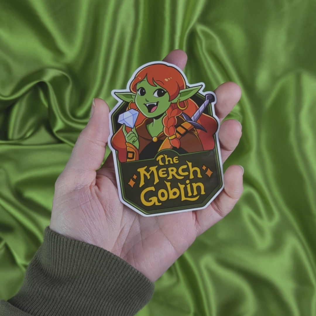 Video of sticker of a happy green goblin woman with long red hair, wearing armor and holding a diamond with text that says The Merch Goblin
