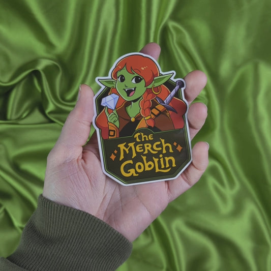 Video of sticker of a happy green goblin woman with long red hair, wearing armor and holding a diamond with text that says The Merch Goblin