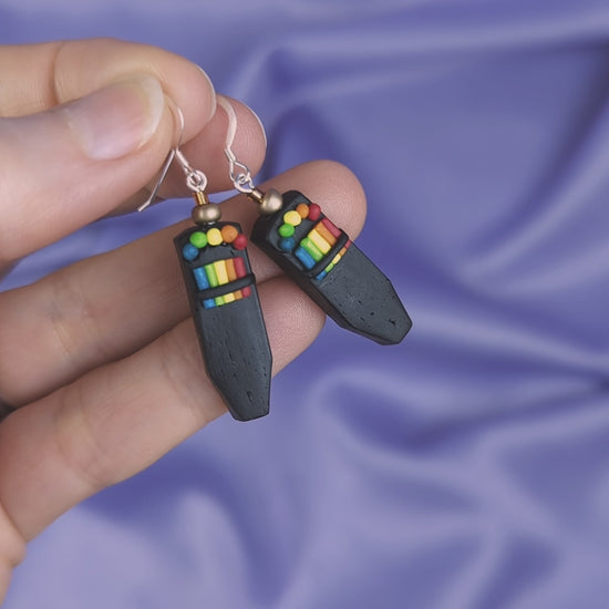 Video of  a hand holding a pair of polymer clay EMF earrings against a purple fabric background