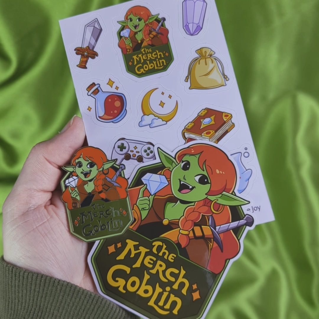 Video of a 3 Item bundle of The Merch Goblin logo sticker, hard enamel pin, and a sheet of fantasy themed stickers including a sword, purple gem, potion bottle, moon game controller, magical book, sparkling jewelry, cute water sprite, flying key, a gold bag