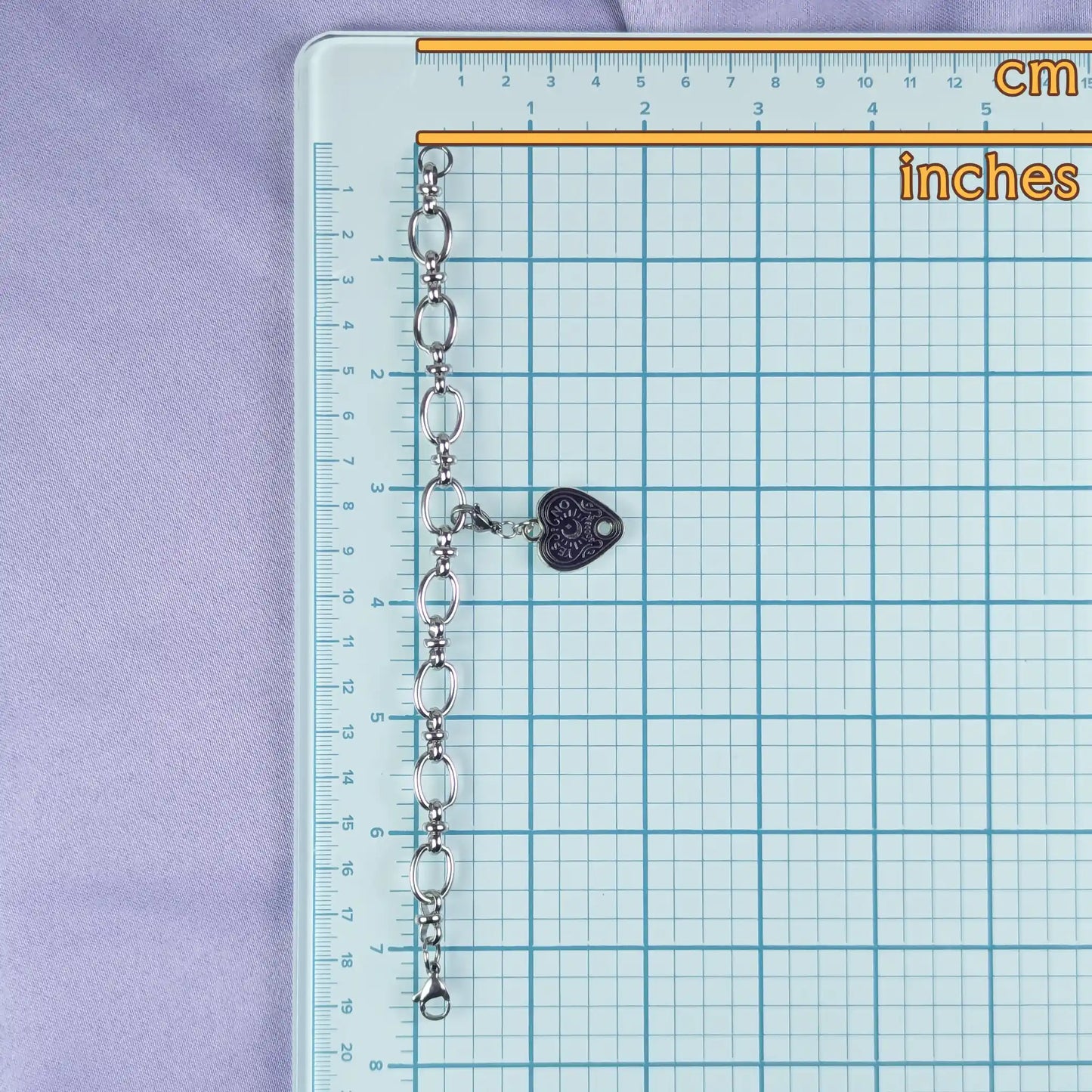 Chain with a heart-shaped charm on a grid ruler with measurements in cm and inches.