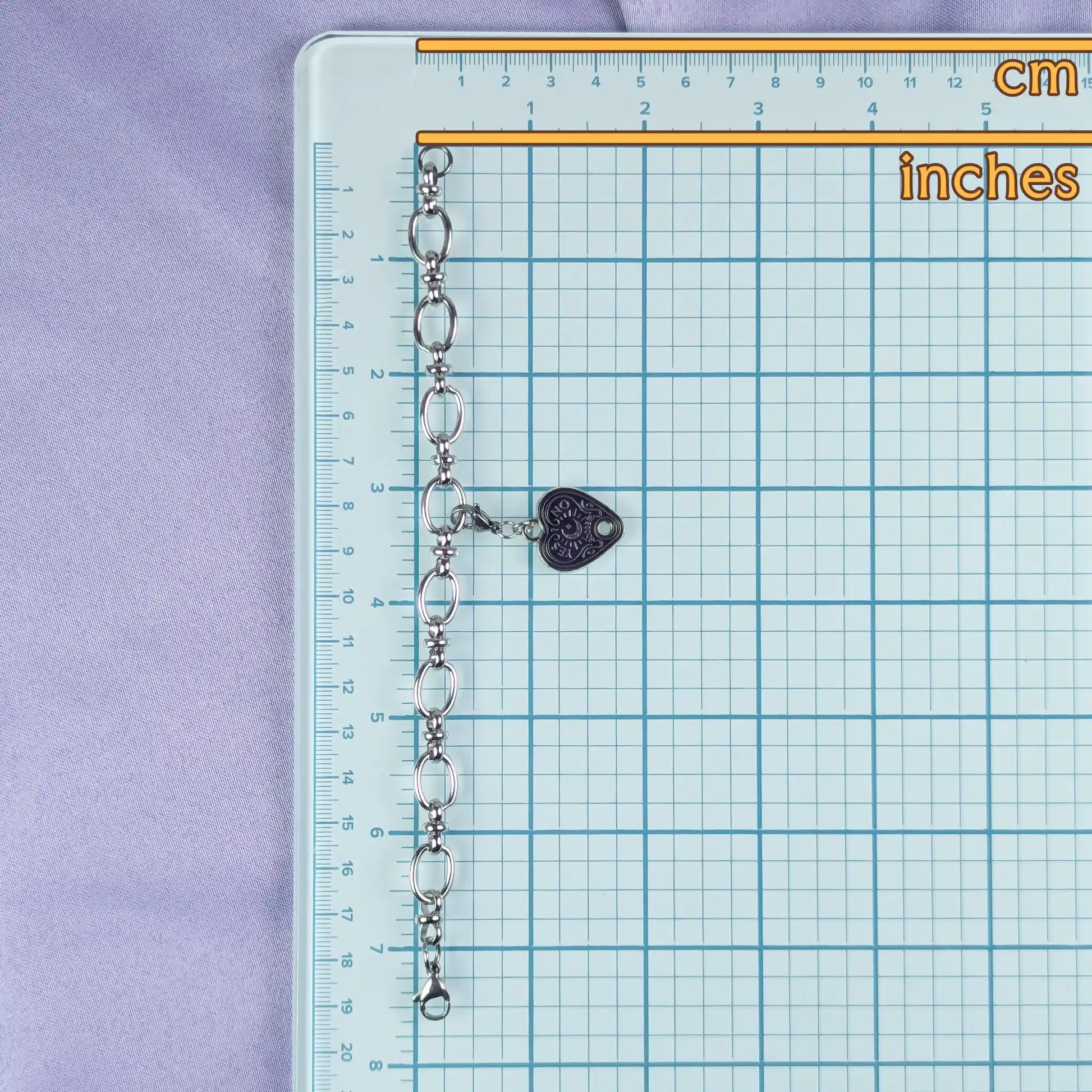 Chain with a heart-shaped charm on a grid ruler with measurements in cm and inches.