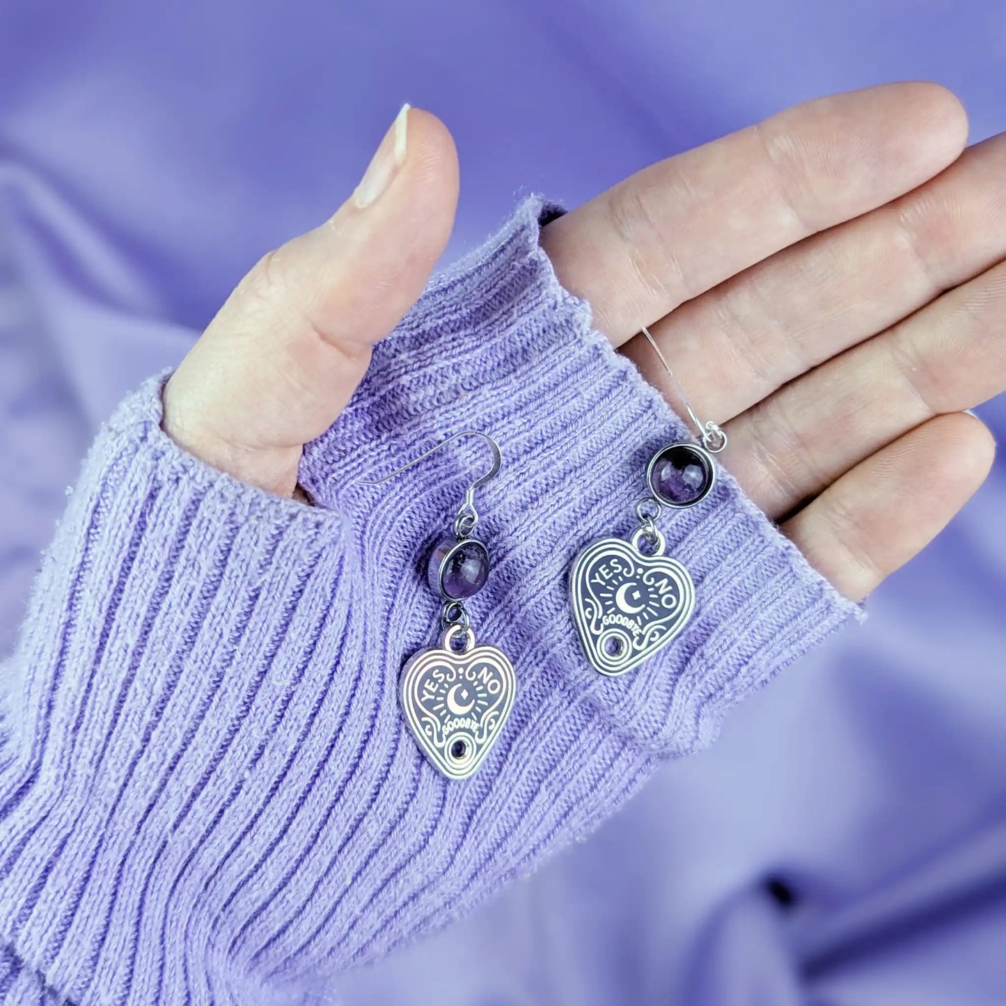 Sterling silver earrings with heart-shaped spirit board pendant and purple amethyst gemstone held in a hand