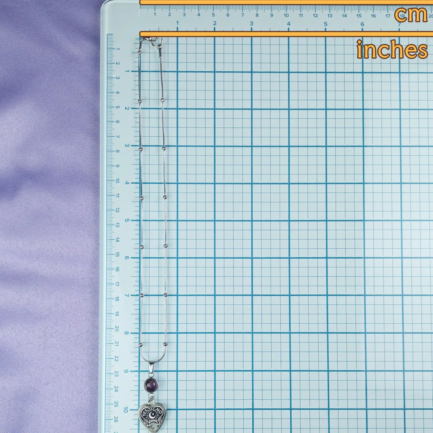 Necklace with heart-shaped pendant on a grid background with measurements in cm and inches.
